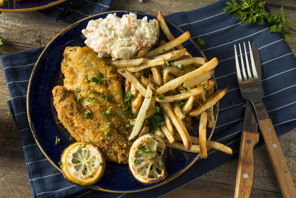 a photo of friend fish with French fries and Cole slaw on a blue striped tablecloth