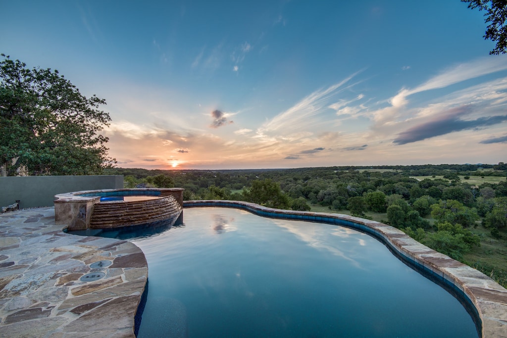 Sunset over the tree filled Guadalupe River Valley. The properties lovely pool and hot tub are in the foreground and have an amazing view of the valley. This is one of the best Airbnbs in San Antonio Texas. 