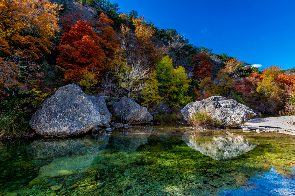 clear water pool with large boulders and colorful trees