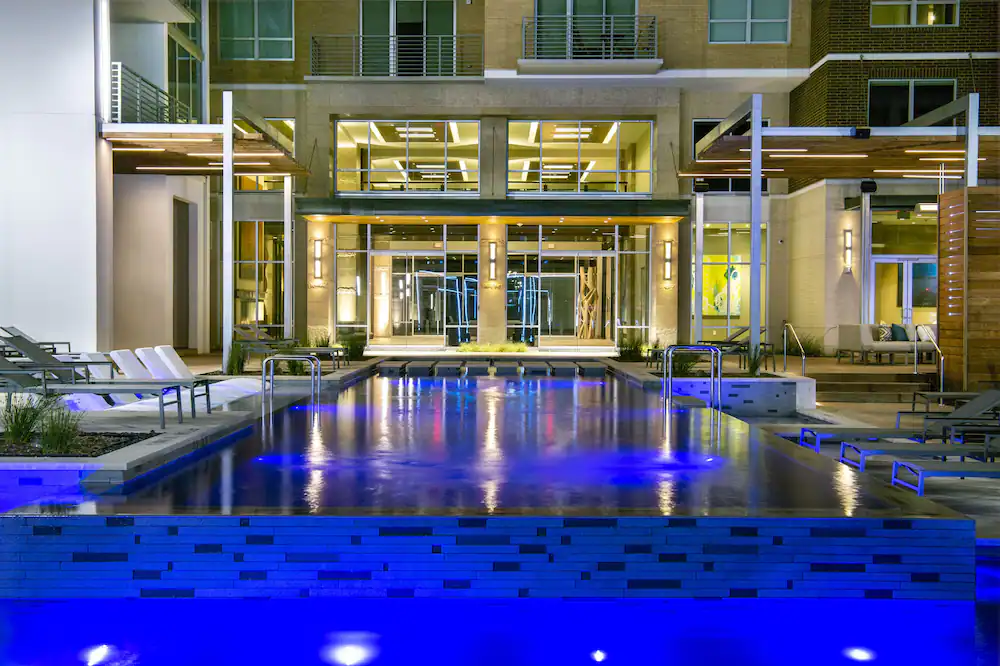 A bright blue swimming pool outside a hotel with white chairs around it