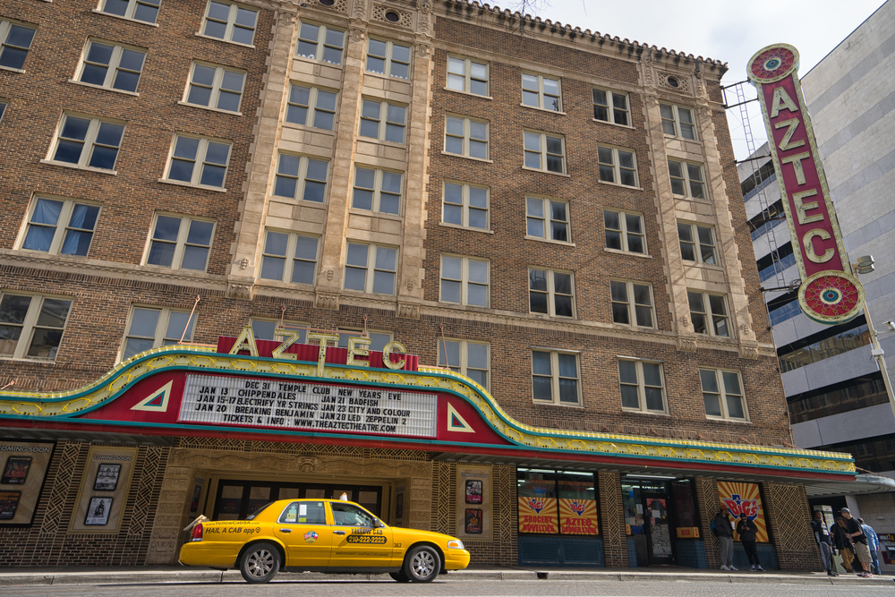 The outside of The Aztec Theatre with a yellow cab outside