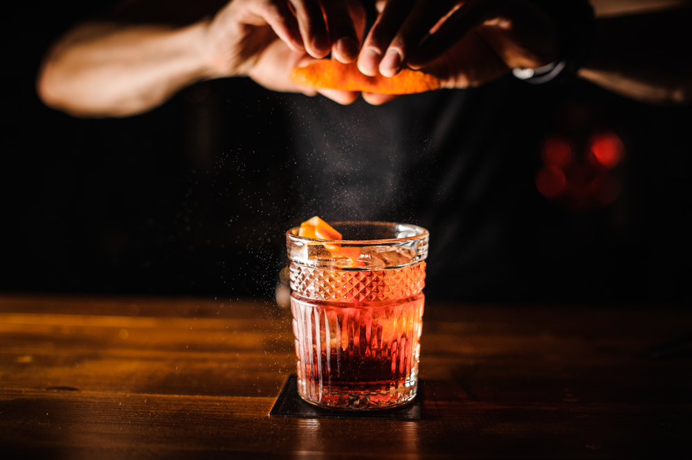 bartender preparing a cocktail and adding an orange peel to it