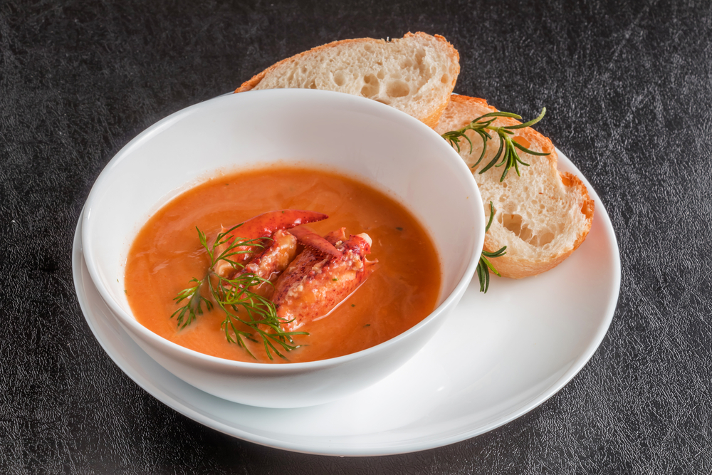 lobster bisque served in a white bowl along with bread on a plate