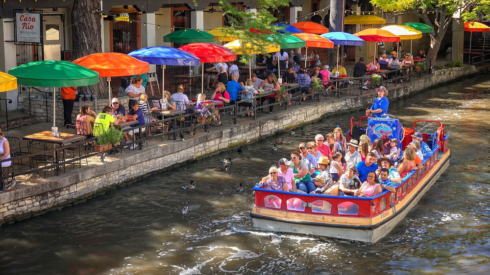 people sitting on a river boat passing by a restaurant san antonio riverwalk
