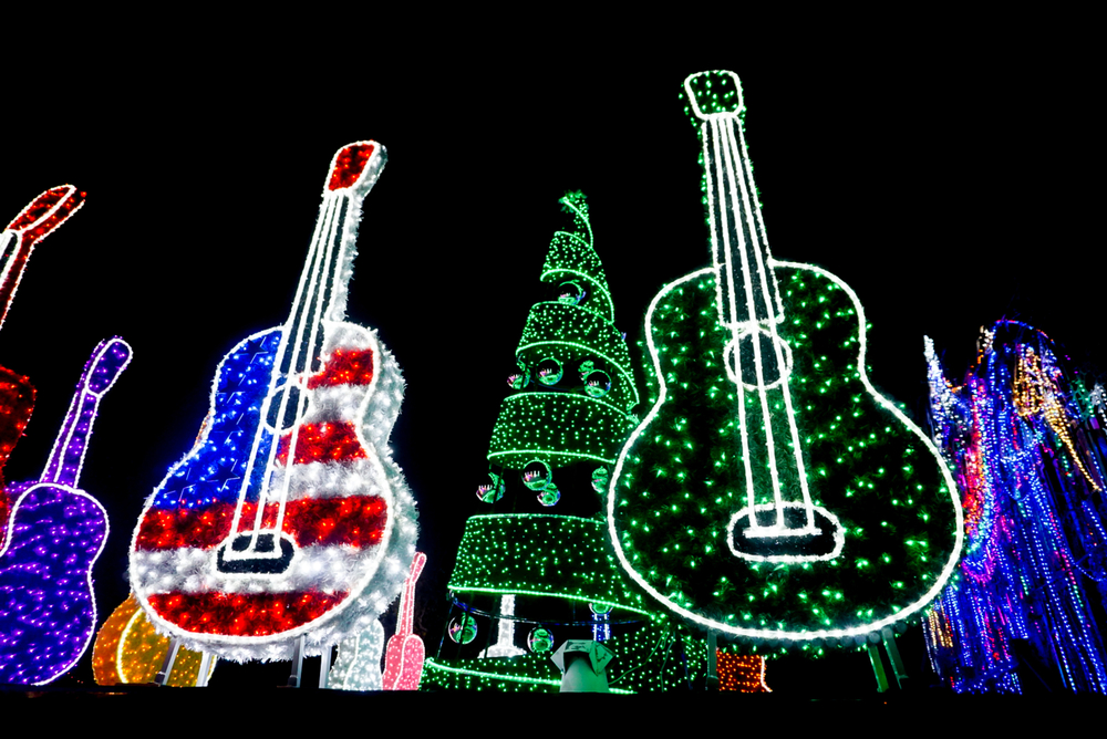 A photo of two Christmas light displays shaped as guitars with colorful Christmas lights and tree in the background.