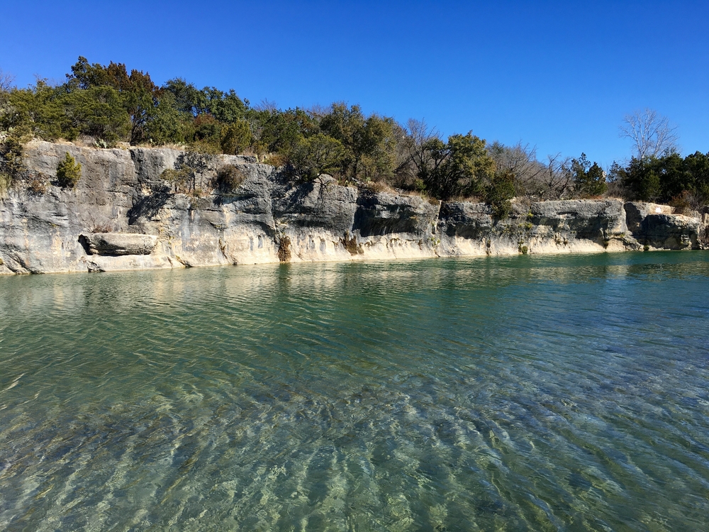 A rocky coastline with trees and clear blue water in the foreground on a sunny day