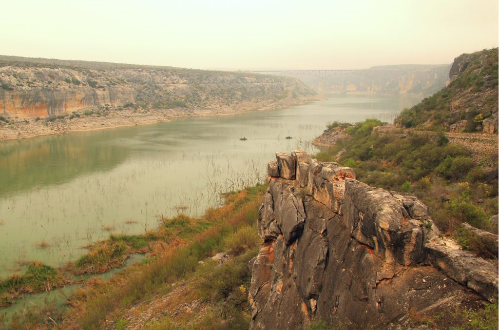 misty view of water from overlook with rocky cliff in the foreground and rocky cliffs on the other banks on the water