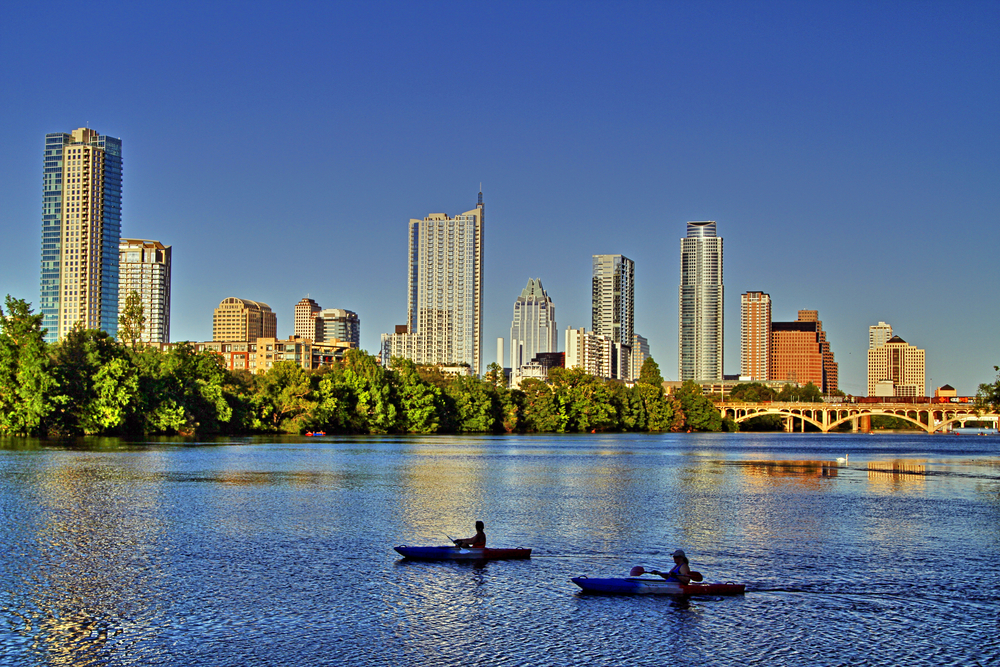 Two Kayakers on a lake with view of trees, and bridge and large buildings in the background at one of the best lakes in texas