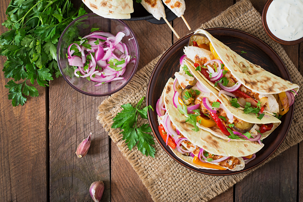 Three chicken tacos served next to a bed of cilantro and red onions.