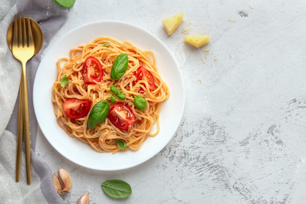 Spaghetti served in red sauce and topped with grape tomatoes and basil on white table at a restaurant in Fredericksburg Texas.