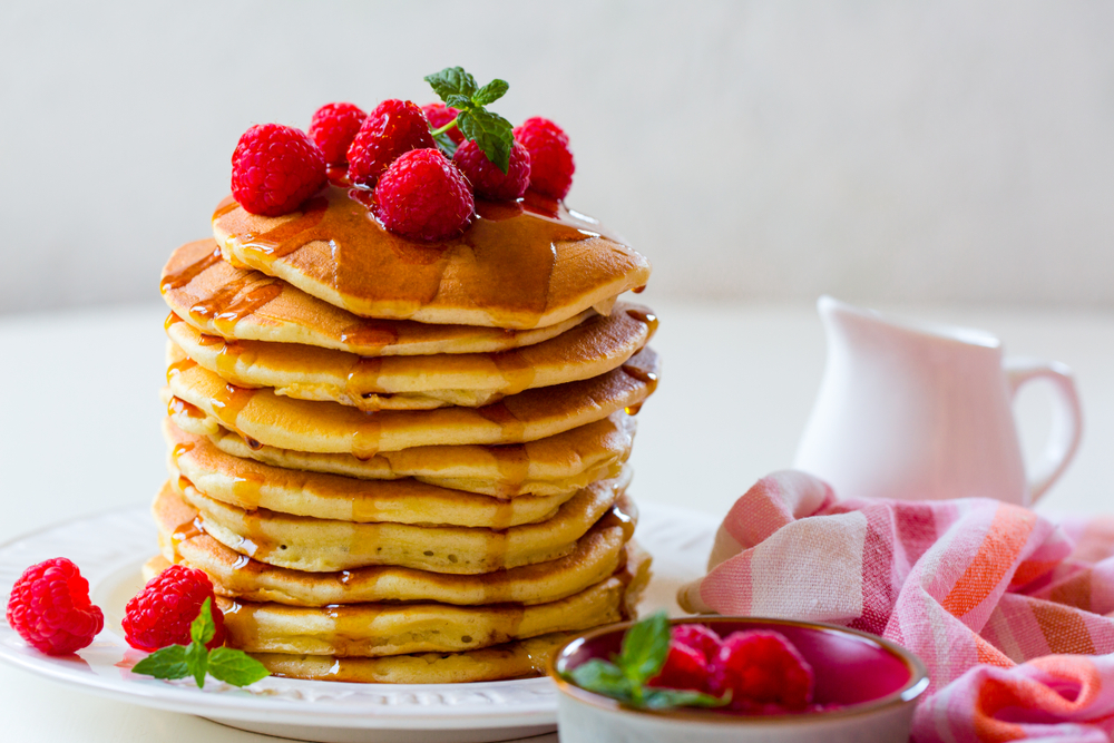 A tall stack of pancakes with raspberries. Get your fill of pancakes at one of the best restaurants in San Antonio: Snooze an A.M. Eatery