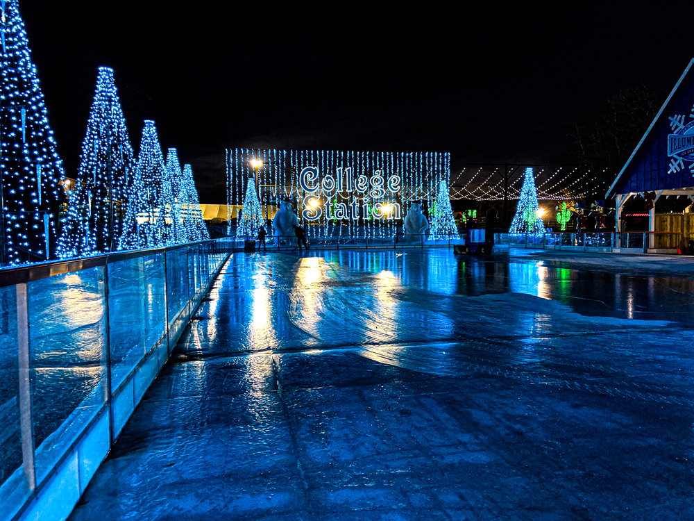 A picture of an ice skating rink reflecting blue light from the surrounding Christmas lights and decorations.