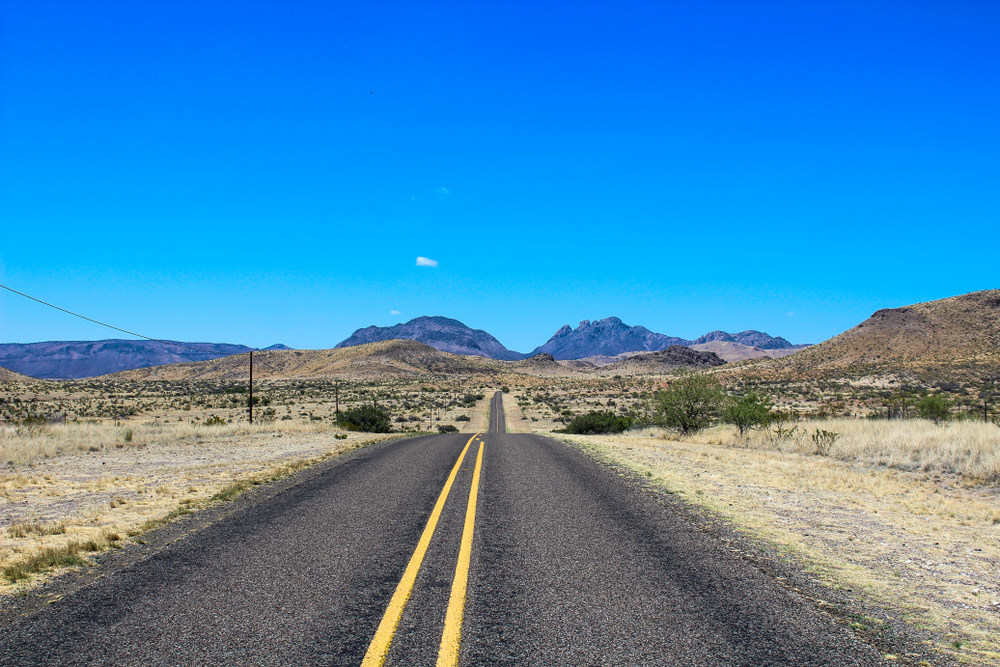 long empty paved road surrounded by desert landscape on a sunny day