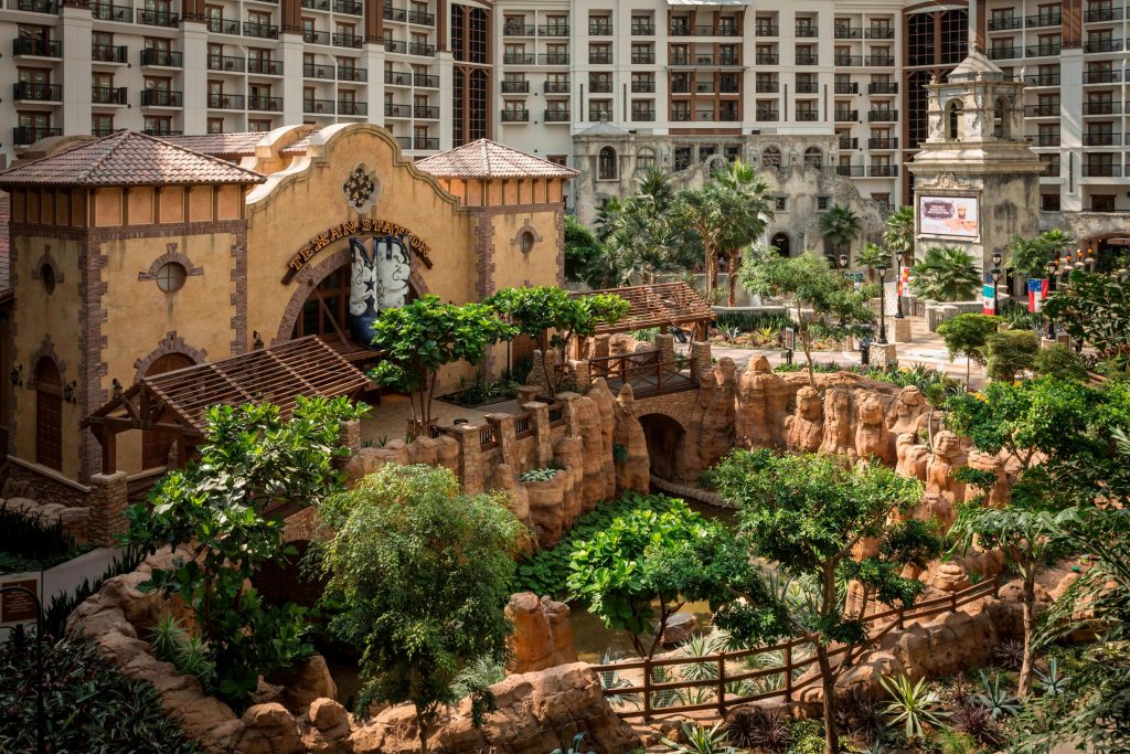 An indoor garden with fully grown trees and walkways sits in the center of the Gaylord Texan Resort with multiple stories of hotel rooms surrounding it. 