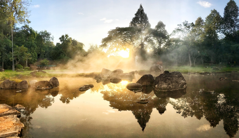 Steam rises from an outdoor natural hot spring at sunrise. 