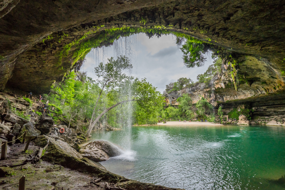 The scenic view of a small waterfall cascading over the mouth of a cave into a grotto filled with aqua water makes Dripping Springs one of the most refreshing weekend getaways from Dallas. 