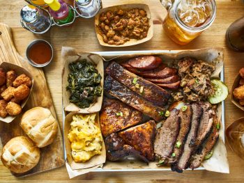 A view of a large barbeque spread like one you can get at some restaurants in Amarillo. There is brisket, ribs, sausage, pulled pork, and grilled chicken. You can also see rolls, collards, mac and cheese, hushpuppies, and glasses of sweet tea.