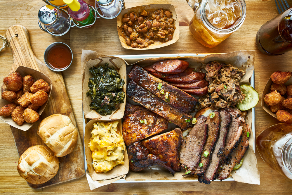 A view of a large barbeque spread like one you can get at some restaurants in Amarillo. There is brisket, ribs, sausage, pulled pork, and grilled chicken. You can also see rolls, collards, mac and cheese, hushpuppies, and glasses of sweet tea. 