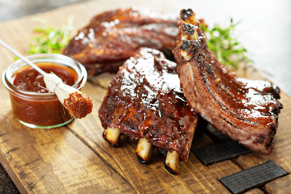 Savory BBQ ribs served with an extra side of BBQ sauce on a wood platter in at a restaurant in Fredericksburg.