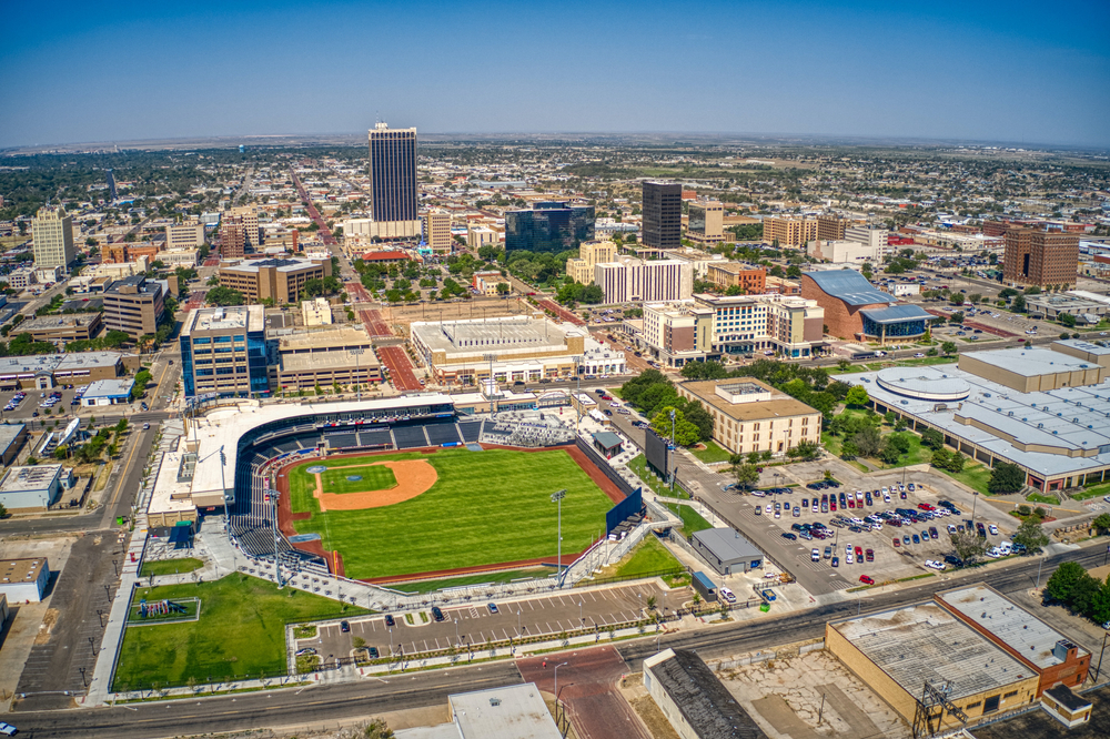 An aerial view of the city of Amarillo Texas. You can see a large baseball diamond, some tall buildings, and the town goes on for miles in the distance.