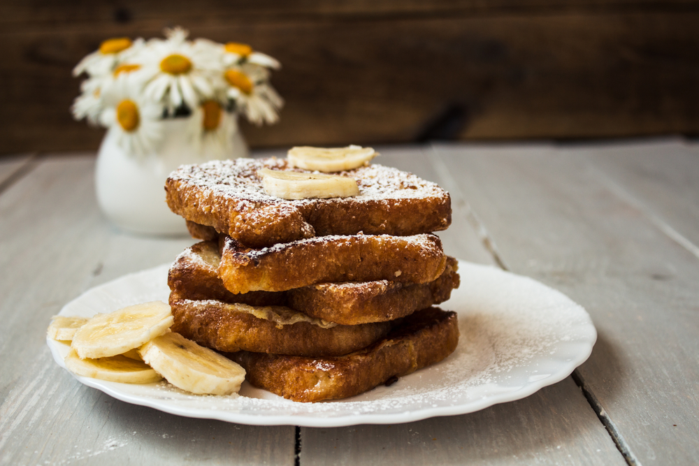 Bananas and french toast served on a white plate, topped with powdered sugar .