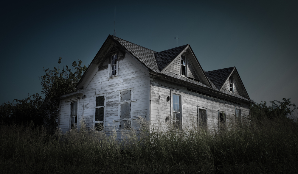 A scary old white abandoned house with broken windows and high uncut grass one of the most haunted places in texas