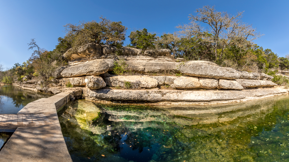 Rocks around a deep pool with trees on top of the rock.