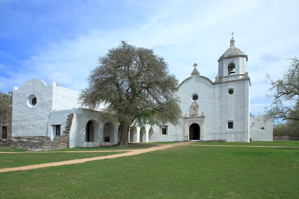 one of the white walled missions in Texas on a green lawn with wispy clouds