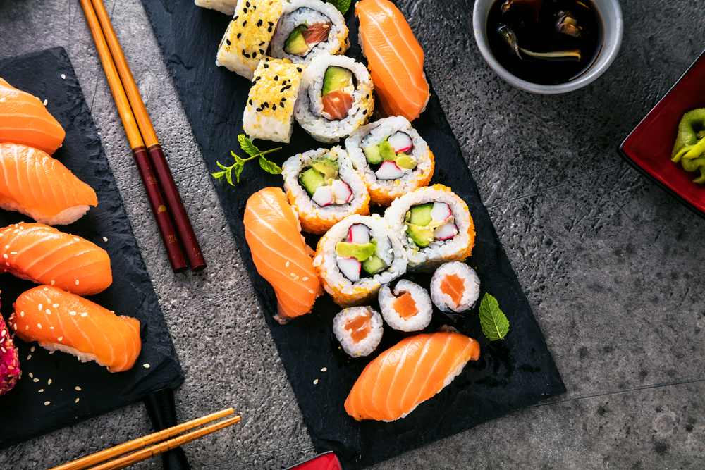 A black stone slab and part of a black stone slab covered in different sushi and sashimi rolls. You can see chopsticks, a small bowl of soy sauce, and the grey stone table. Its one of the best sushi restaurants in Austin. 