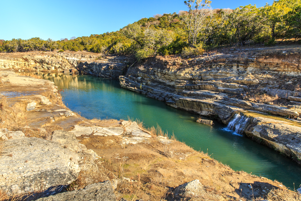 canyon lake surrounded by a rocky shoreline with a small waterfall flowing on a sunny day