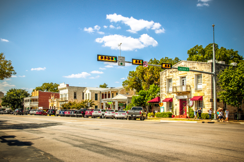 People walking in front of the Rathskeller Restaurant set in a small town with cars parked and a street light overhead on a sunny day