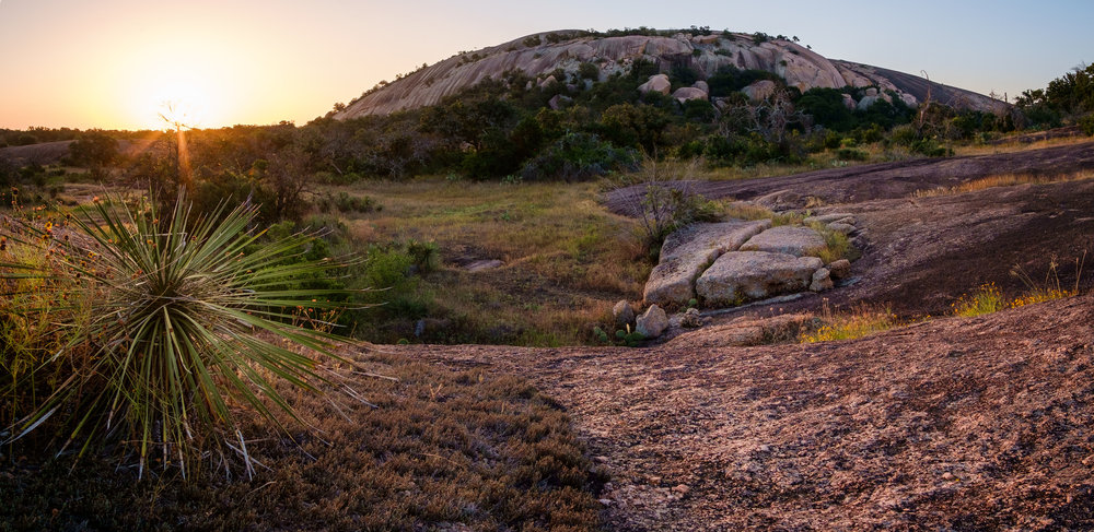 a large rock hill at sunset surrounded by sparse greenery one of the best things to do in texas hill country