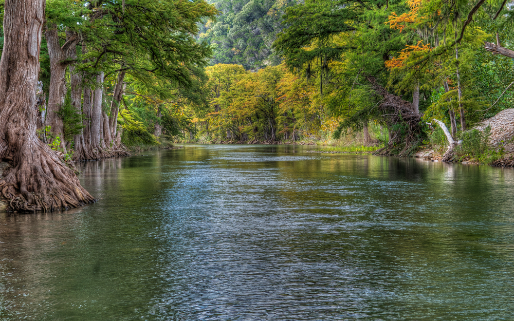 one of the top places to visit in Texas Hill Country, a wide river with large leafy trees on either side