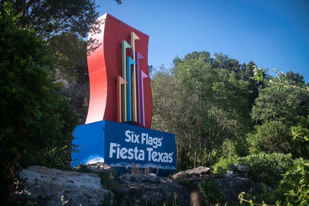 Sign for six flags fiesta amusement parks in Texas with trees and water surrounding.