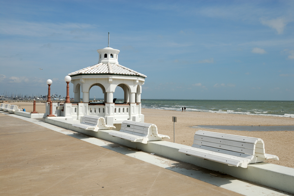 white benches on Corpus Christi Beach in front of a white gazebo with the beach in the background.