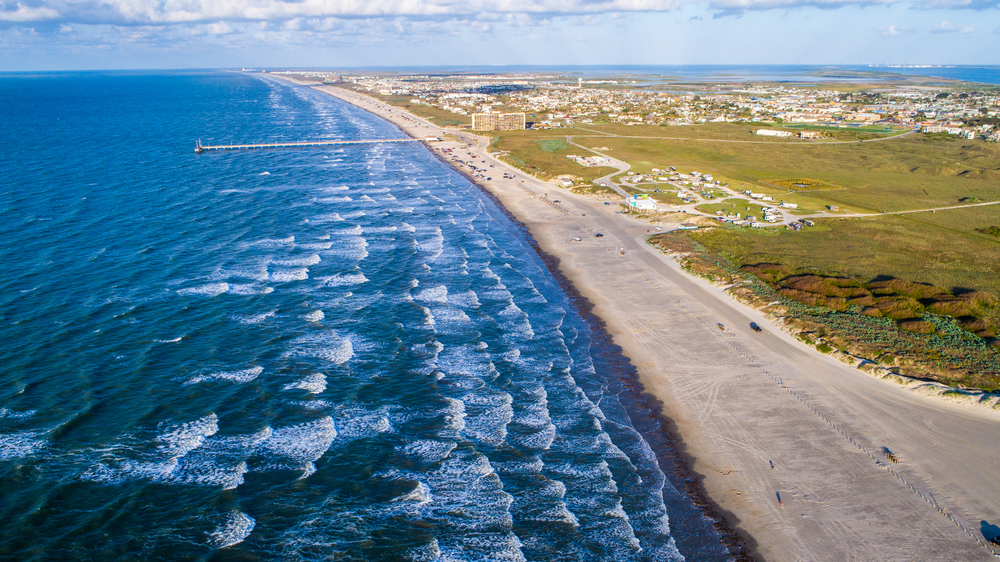 an aerial view of a beach with rough waves crashing and a boardwalk in the distance