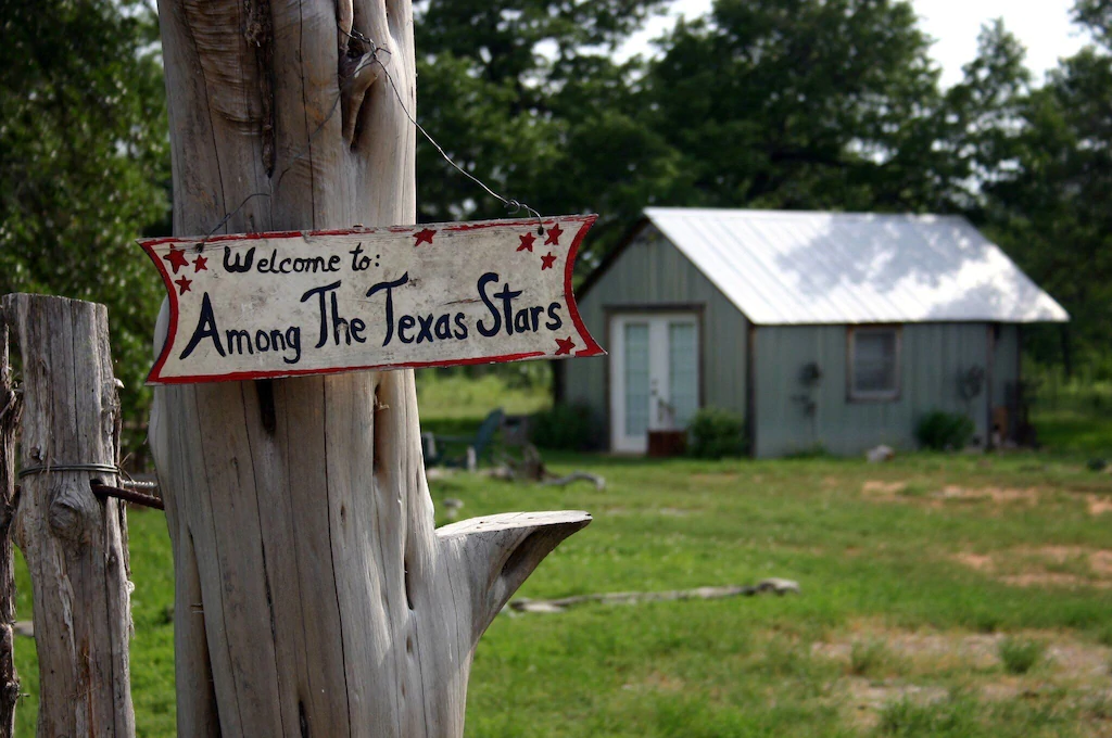 A welcome sign to the Among the Texas Stars cabin, one of the best rentals in Fredericksburg, with the cabin in the background. 