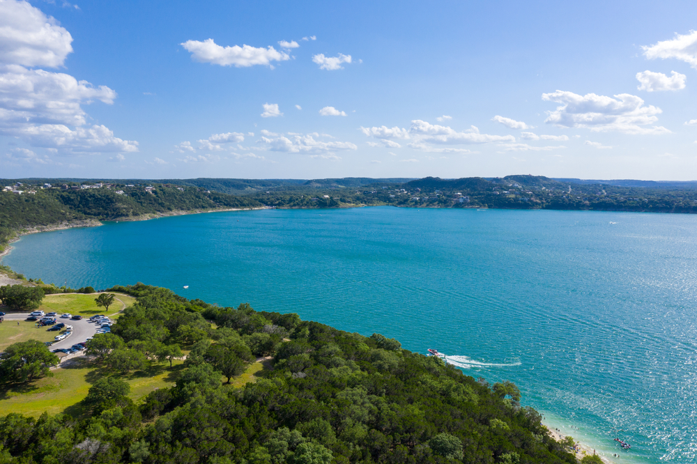 aerial view of teal lake surrounded by trees on a bright sunny day