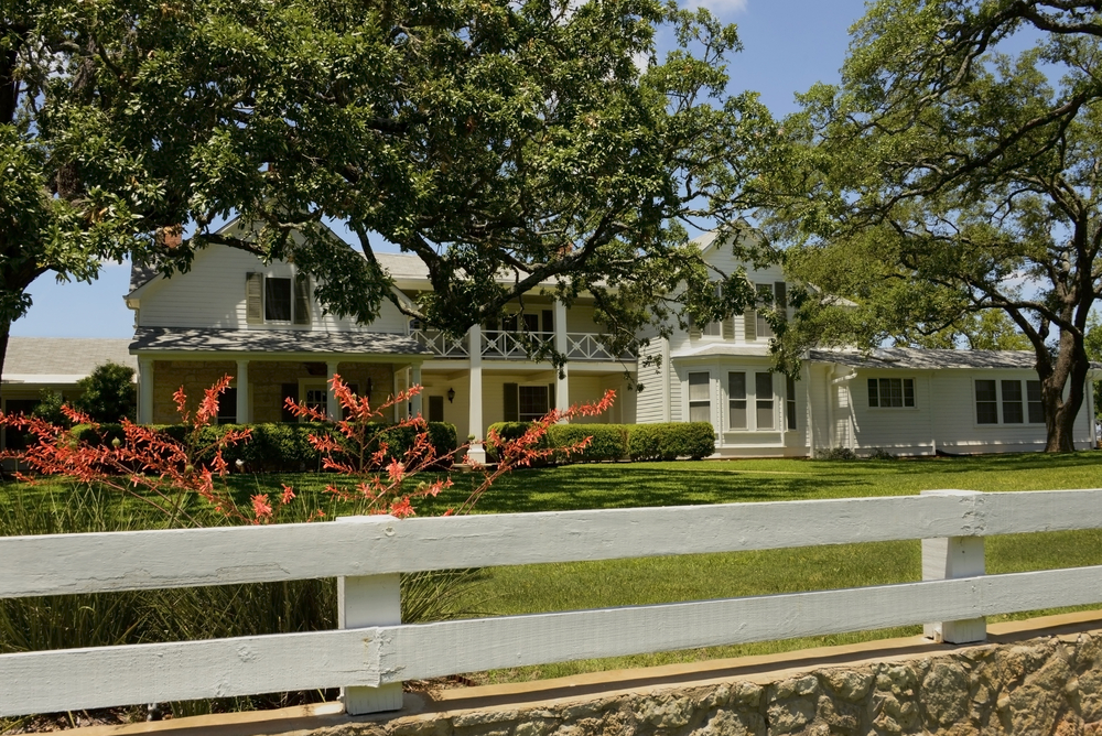 a large beautiful two story home with trees in the yard behind a white fence