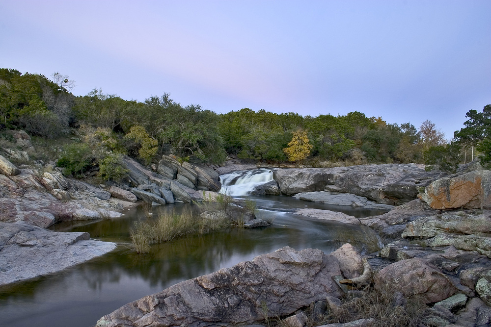 Medium sized spring flows over a rocky landscape surrounded by trees at Devil's Waterhole.