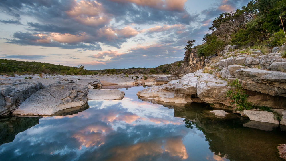 Small spring in a rocky landscape reflects the sky and clouds in Pedernales Falls State Park, a pretty swimming hole near Dallas.