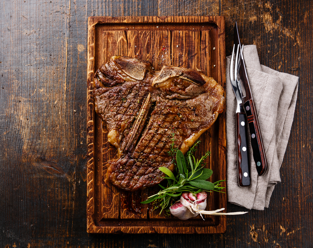 Large T-bone steak sitting on wood board with fork and knife being served at restaurant in El Paso