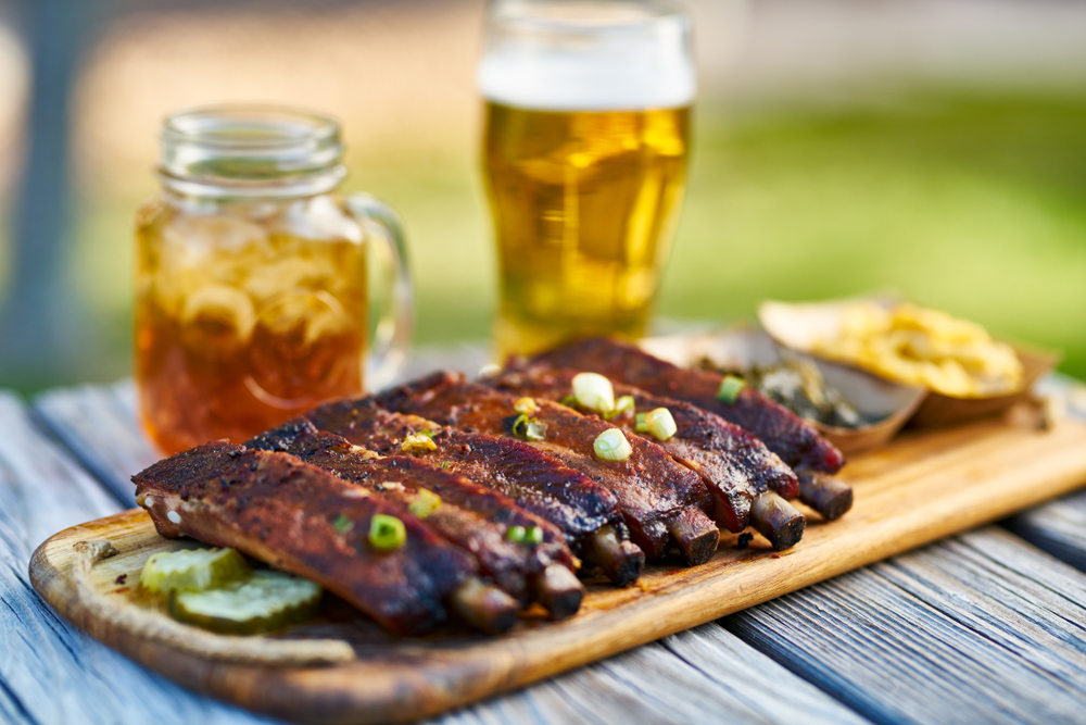 rack of ribs sitting on wood plate with glass of tea and a beer in the background
