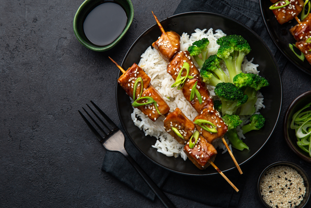 Bowl of white rice with broccoli and tofu skewers.