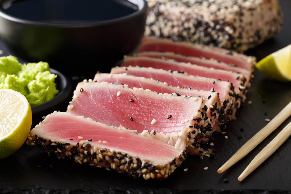 Ahi tuna slices next to some chop sticks and a bowl with guacamole.