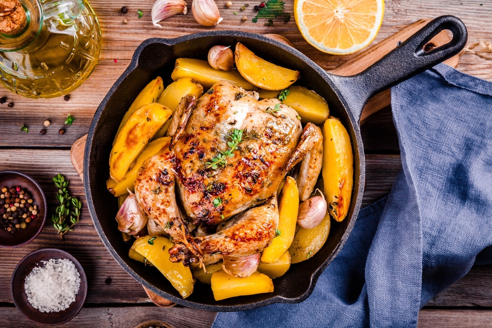 Cast iron pan filled with chicken and squash surrounded by spices and a bottle of oil on a wooden table at the Cast Iron Grill, one of the best restaurants in Lubbock.