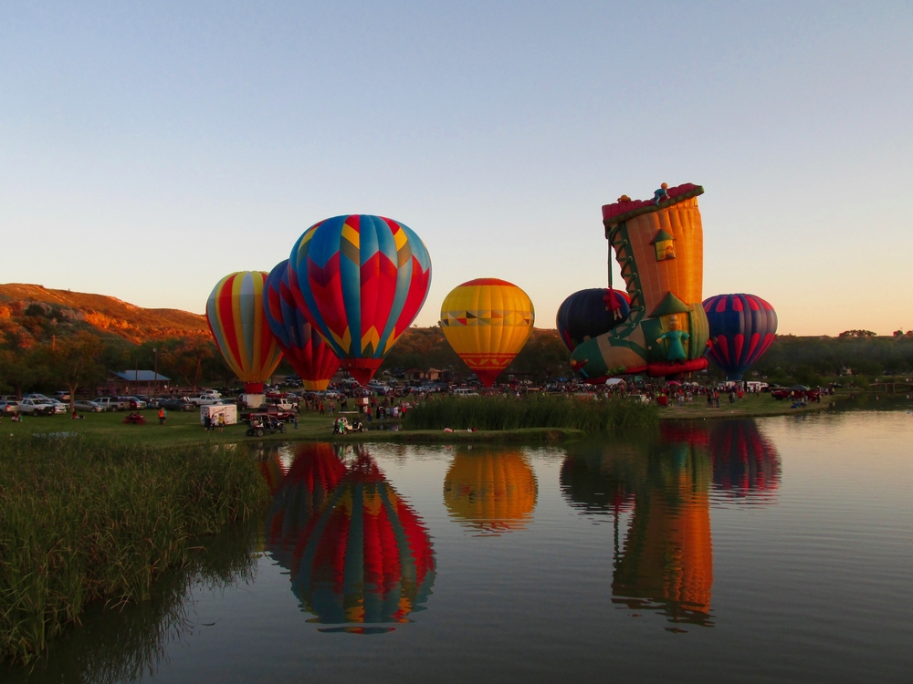 Hot air ballons next to a lake in front of hills in Lubbock, TX.