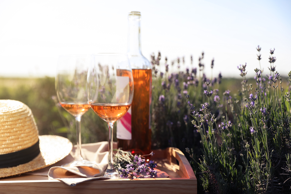 Two wine glasses and a wine bottle sit on a table with a hat in a field of lavender at a wineries In Fredericksburg