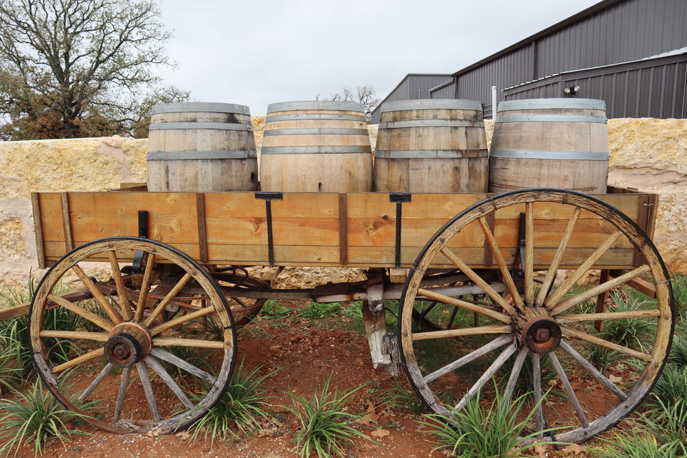 Wagon carrying 4 wine barrels in front of rock wall, near wineries in Fredericksburg