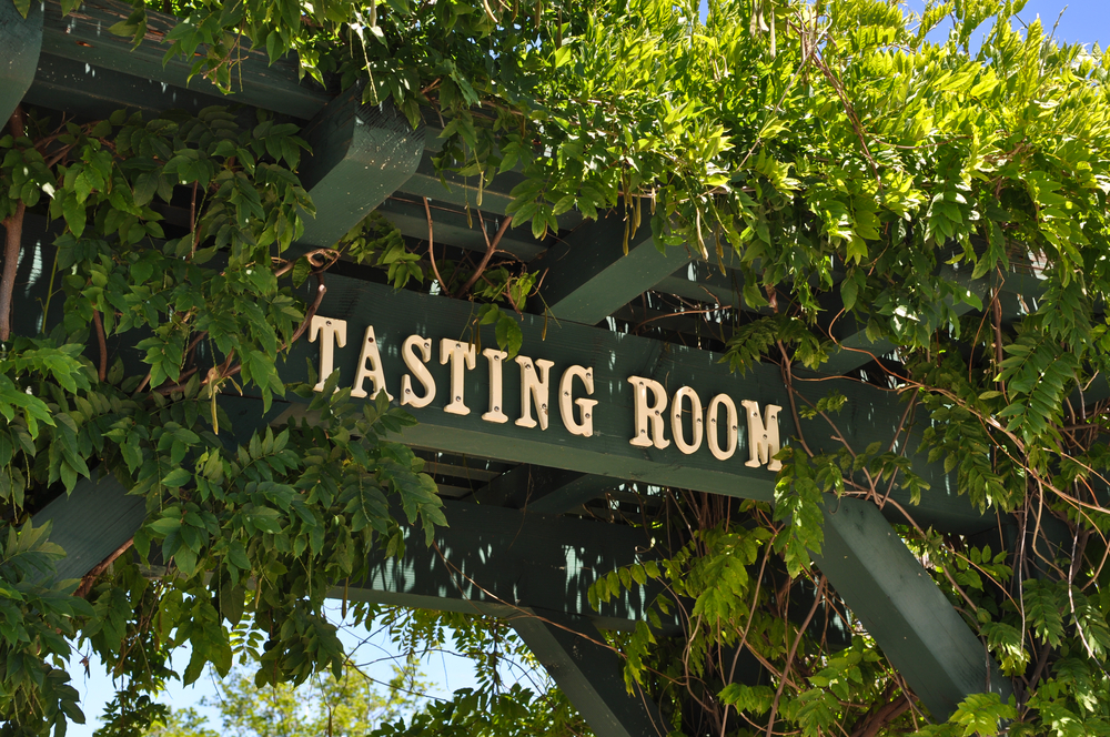 overhead sign reads tasting room covered in vines in front of a wineries in Fredericksburg
